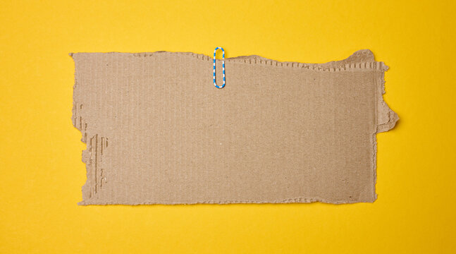 Torn piece of brown cardboard with a blue and white paper clip on a yellow background.