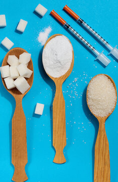 Sugar spoons and insulin syringes on a blue background symbolize the risk of diabetes and addiction to sweets.