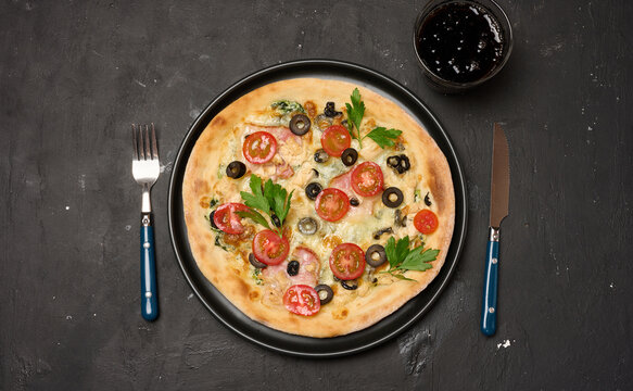Whole baked pizza with chicken and cheese in a round plate on a black table