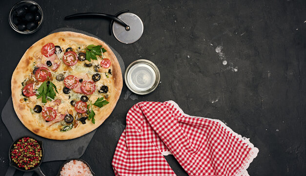 Baked pizza with chicken, tomatoes and olives on a black table, top view