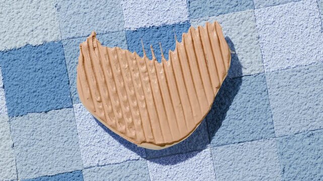 Overhead shot of a smeared beige foundation blob shaped like a heart generates a lively shadow on a blue powder mosaic surface made of squares | Creative concept for a foundation commercial