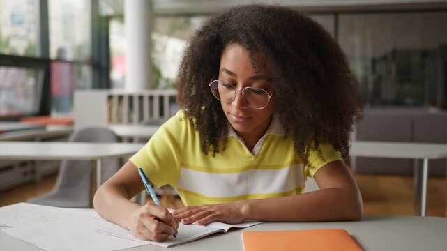 Focused African American student girl writing in textbook preparing for exams female woman studying write knowledge educate process study learning at table in high school learn in college university