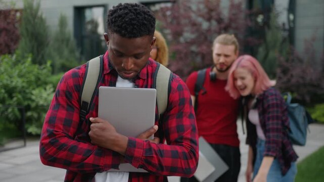 Group of aggressive students bullying African American student guy unhappy feeling shame in city ethnic man male upset with mockery bully multiracial classmates laughing discriminate at university