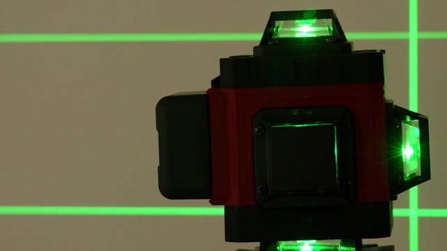 Green laser pointer emits bright light. Black and red device parts are visible. Laser beams form a grid pattern. Technical setup highlights precision equipment