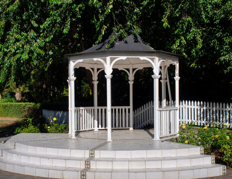 White wooden gazebo surrounded by lush foliage in a sunny park