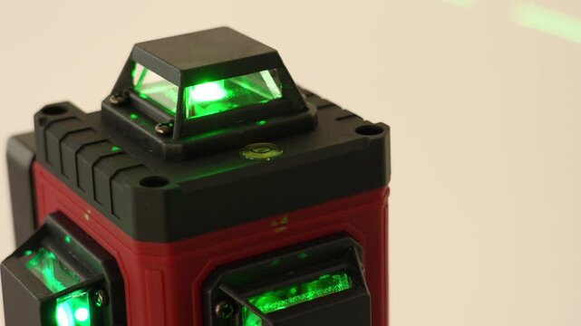 Close-up of red and black laser level with green lasers. Clear beams highlight precise measurement capabilities. Single keyframe shows device details. Used for construction alignment tasks