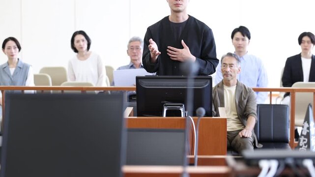 法廷で証言を行う若い男性と裁判を見守る傍聴人　