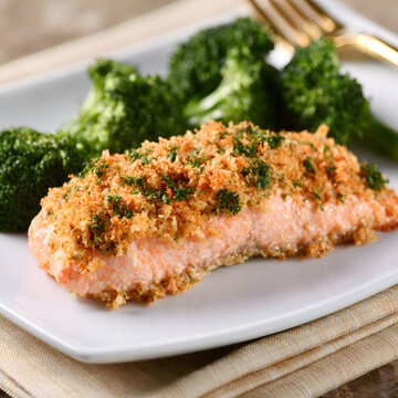 Baked with a garlic parmesan crumb topping, the salmon fillet is a crispy and healthy gourmet meal served with broccoli on a white plate