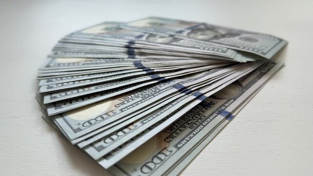 A wide fan of 100 dollar banknotes neatly arranged on a white surface creates a clean financial composition. Ideal visual for wealth, prosperity, investment, banking, budgeting and cash concepts.