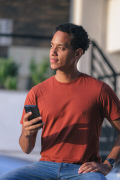 Man sitting outdoors holding a phone while looking up and smiling