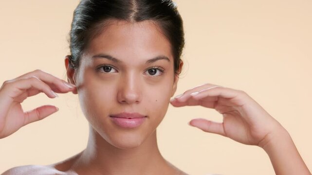 Closeup of youthful woman touching her chin with dorsum of both hands on beige bg | Cosmetic footage revealing skin purity concept