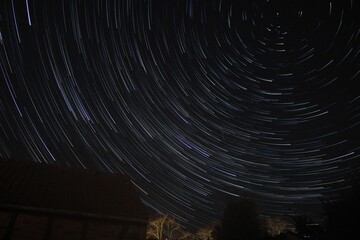 Sternspuren (Startrails) am Nachthimmel über der dunklen Landschaft