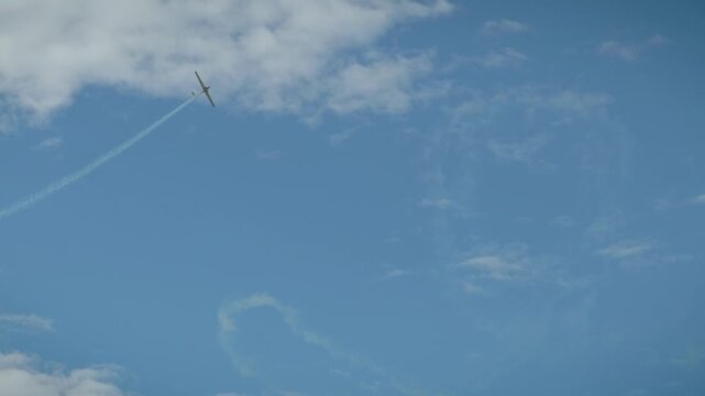 A white smoke loop pattern created by an aerobatic airplane in a clear blue sky with soft white clouds.