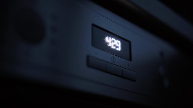 Close-up digital clock display glowing on dark appliance panel with soft blurred foreground and moody low light