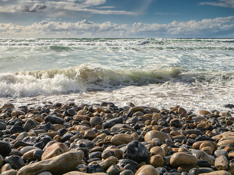 Dark storm clouds hover over wild ocean, . Waves crash against rocky shore. Turbulent water flows toward distant hills. Nature power displayed in dramatic weather. Strandhill beach, Sligo, Ireland.