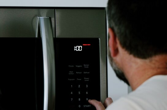 Man setting digital clock time on kitchen microwave stove appliances, representing changing clocks - daylight savings time, spring forward, fall back