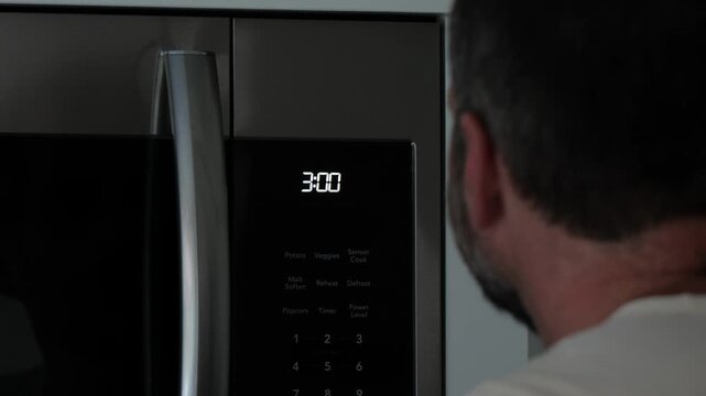 Man setting digital clock time on kitchen microwave stove appliances, representing changing clocks - daylight savings time, spring forward, fall back