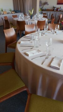 Elegant restaurant dining room with fully set tables, glassware, napkins, wooden chairs, floral accents