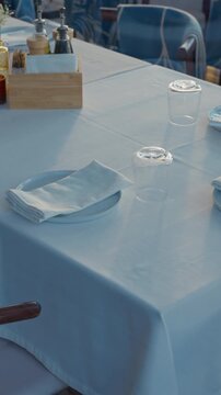 Elegant restaurant table setting with white tablecloth, folded napkin on plate, glassware and condiment bottles