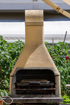 Outdoor stone barbecue fireplace with electric grill inside placed in green garden during sunny summer day in house yard in Italy concept.