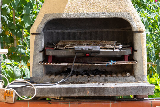Outdoor stone barbecue fireplace with electric grill inside placed in green garden during sunny summer day in house yard in Italy concept.
