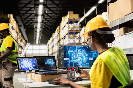 A young Black worker scans AWB labels next to AI tools on a PC, registering shipment details and airway bills for express delivery in logistics hub.