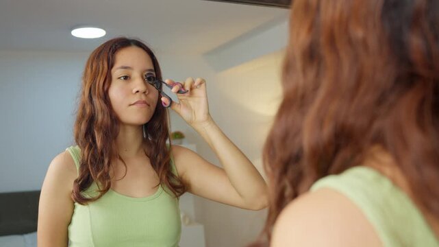 Young woman curling her eyelashes in front of a mirror