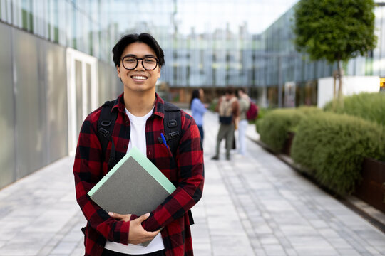 Smiling university student holding books on campus pathway. Copy space.