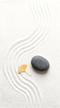 A smooth grey stone and a yellow ginkgo leaf on a traditional zen garden sand