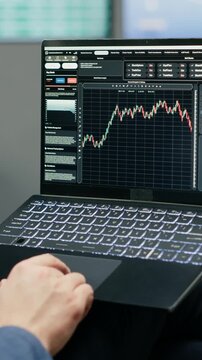 Vertical frame: A business delegate monitors trading data and stock exchange graphs on a laptop in an airport lounge, tracking financial forecasts and investment trends while waiting near the gate.