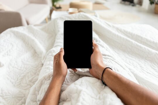 Unrecognizable Person Relaxing At Home In Cozy Bed Under Blanket, Holding Tablet With Blank Screen. Emphasizing Comfort And Leisure In The Bedroom Setting. Digital Lifestyle Concept.