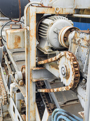 Railroad equipment with rusty gears and motor, showing signs of wear, interconnected components including chain mechanism, light gray painted metal parts peeling off revealing rust, ribbed texture © Mister