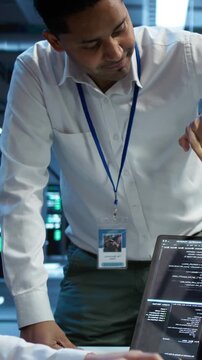 Vertical composition: Admin team tracking network traffic in a high tech server room using computer, connecting infrastructure management, network control and enterprise technology workflow.