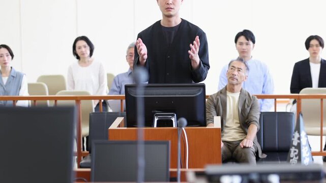 法廷で証言を行う若い男性と裁判を見守る傍聴人　