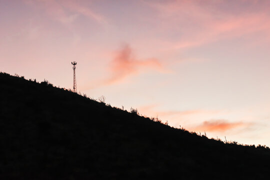 Telecommunication tower silhouette on hillside at colorful sunset sky