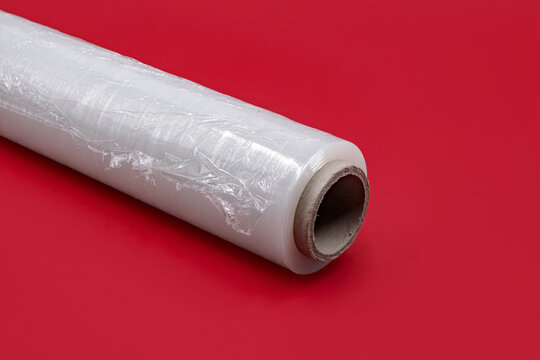 Roll of clear stretch wrap film. Stretch roll on a red background. Useful for packaging, logistics, shipping, moving, and warehouse supply chain concepts.