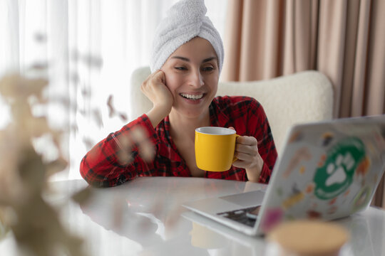 Smiling woman holding hot drink while using laptop at home