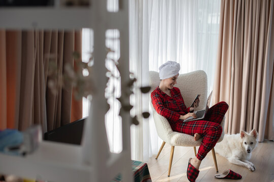 Woman using smartphone and laptop at home with white dog nearby