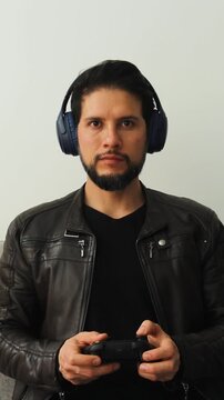 vertical front detailed view of a smiling latin gamer man playing with a wireless controller in a competitive attitude