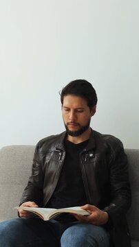 vertical view of a concentrating man reading a text book sitting on a grey couch