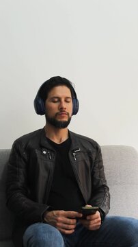 Vertical view of a tranquil man sitting on a couch listening music on a wireless headset