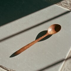 Fototapeta premium Weathered olive wood spoon casting long shadow on pale stone