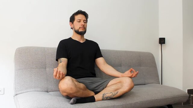 detailed view of a hispanic man sitting at the left side of a couch in the lotus pose meditating