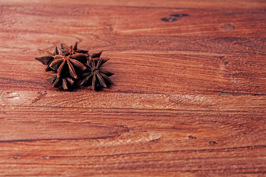 Star anise pods rest on warm wooden surface. Dark brown spice forms star shape. Texture and color highlight natural ingredients. Perfect for food, recipe, or cooking design