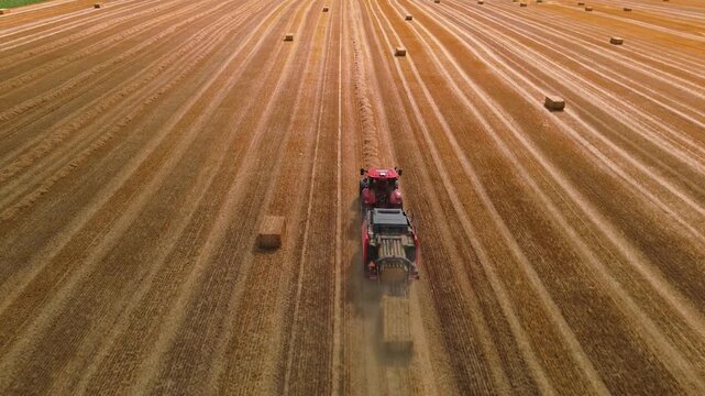 Aerial view of red square baler machinery baling straw on farmland after harvest
