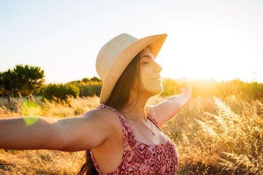 Young woman with closed eyes and arms outstretched embracing a moment of happiness and peace outdoors, feeling the warmth of golden hour sun rays in a summer field