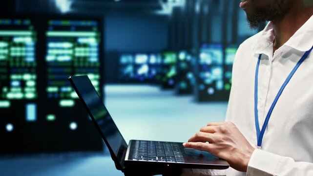 Programmer walks among electronics in a data center, overseeing computing resources, data storage equipment and network operations during through mainframe rows.