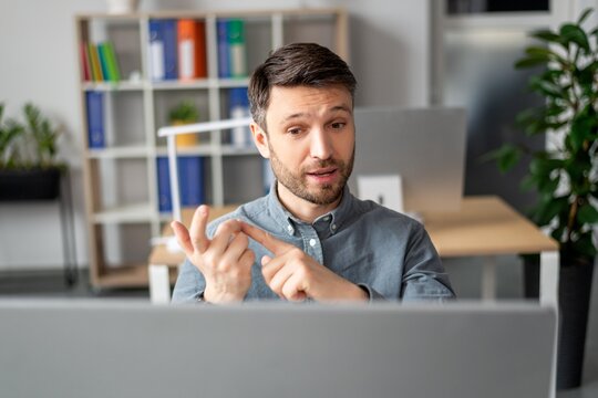Focused Caucasian Male Professional Gesturing While Explaining Ideas During Video Call At Modern Office. Engaged In Discussion, Using Computer To Communicate, Technology, Business Concept.