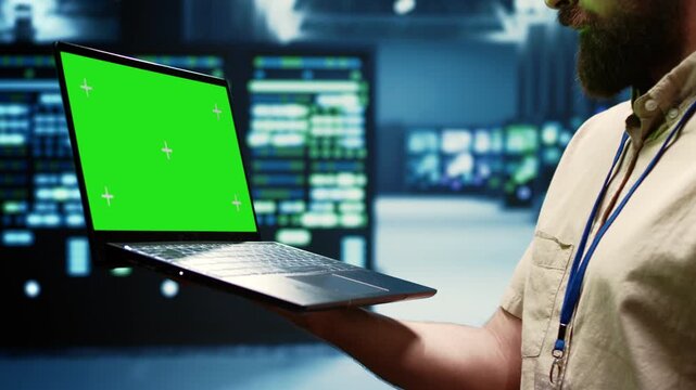 Engineer checks server clusters with a laptop mockup in a data center, keeping the green screen display ready for screen replacement and post production during server check green screen.