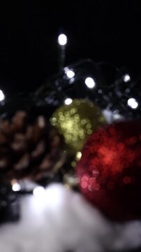 Una toma de cerca de unos adornos de navidad de varios colores con luces de navidad en un fondo negro. Video Vertical